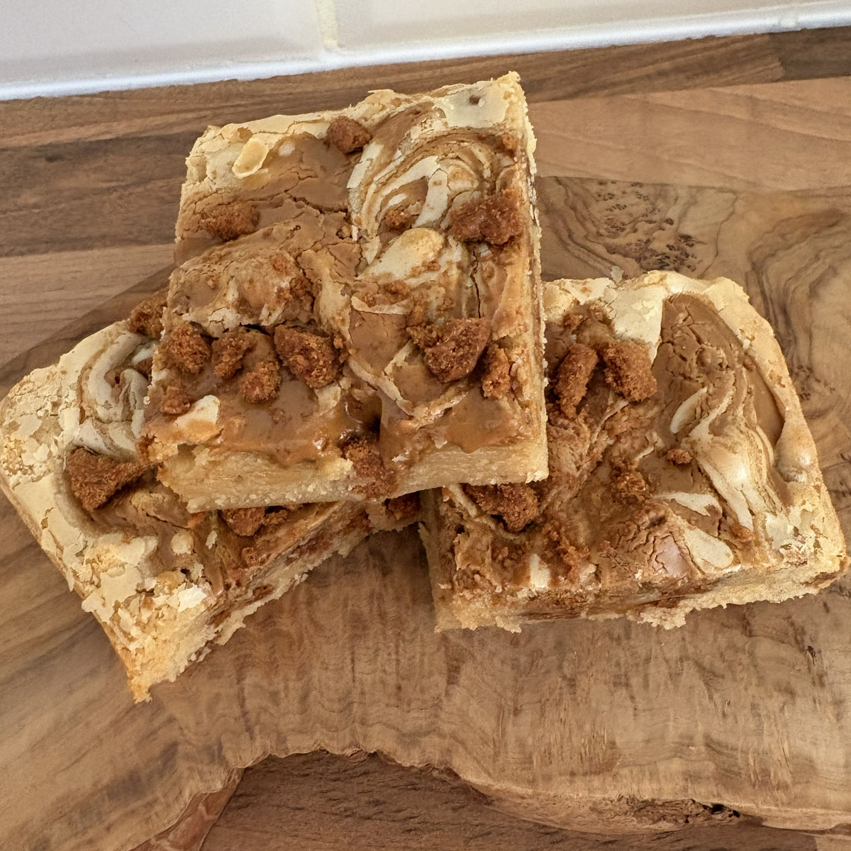 Three square pieces of biscoff blondie on a wooden surface.