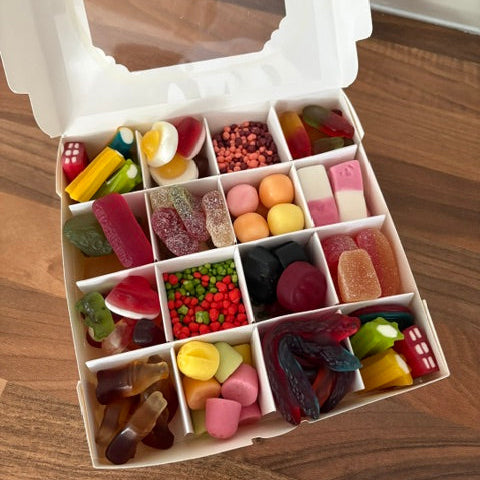 An open white plastic candy organizer box filled with assorted colorful gummy candies, arranged in compartments on a wooden tabletop.