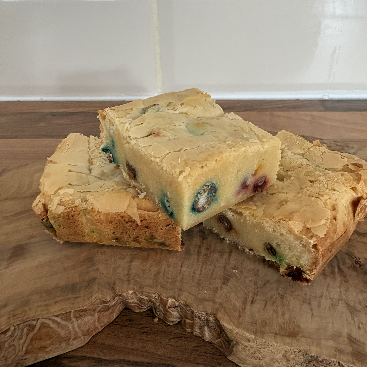 Three pieces of blondie on a wooden cutting board with a tiled wall background