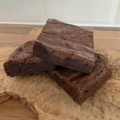 Three Dairy Free Gluten Free Nutella brownies stacked on a wooden cutting board with a tiled backsplash in the background.