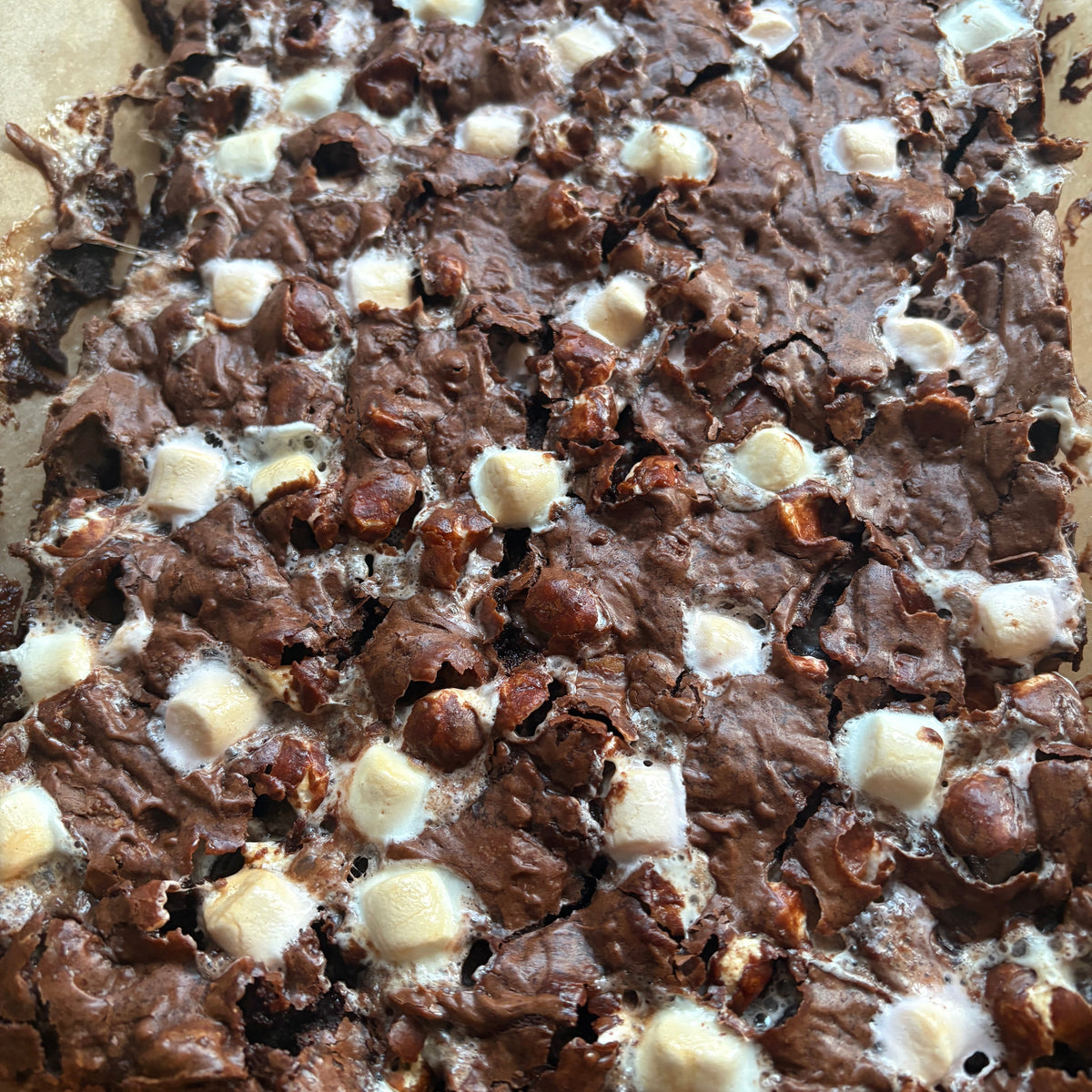 Rocky road brownies topped with melted white marshmallows, photographed close-up in a baking pan.