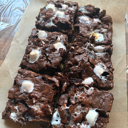 Six chocolate brownies topped with melted white marshmallows, arranged on a sheet of brown parchment paper.
