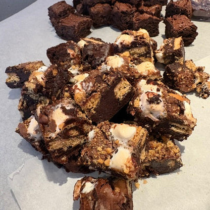 A pile of chocolate brownies and dessert bars mixed with white frosting and crumb cookie pieces, arranged on parchment paper.