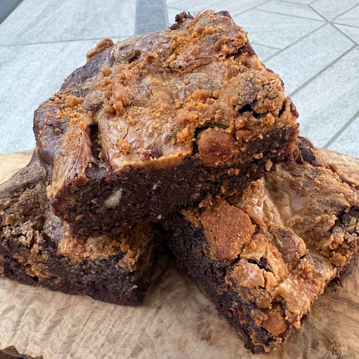 Two freshly baked chocolate brownies with crumb streusel topping, stacked on a rustic live-edge wooden board.