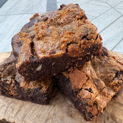 Two freshly baked chocolate brownies with crumb streusel topping, stacked on a rustic live-edge wooden board.