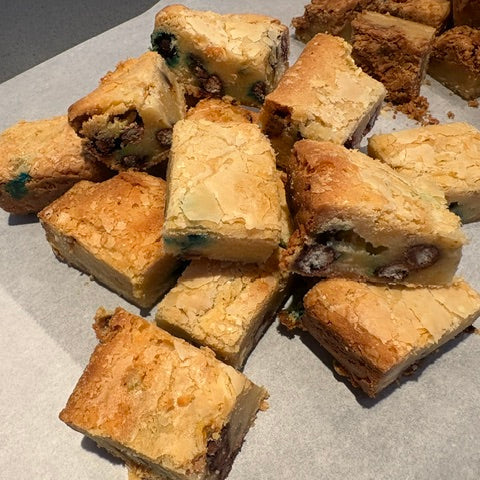 Slices of golden-brown m+m blondie bites arranged on parchment paper.