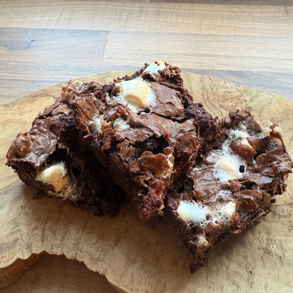 Three chocolate brownies with white chocolate chips stacked on a wooden serving board over a wood floor.