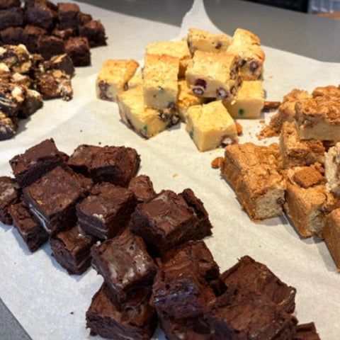 An assortment of freshly cut brownies and fudge pie squares arranged on parchment paper on a kitchen counter.