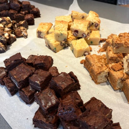 An assortment of freshly cut brownies and fudge pie squares arranged on parchment paper on a kitchen counter.