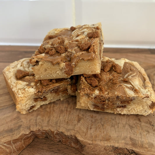 Three Biscoff blondies with crumbled Biscoff biscuits on a wooden surface