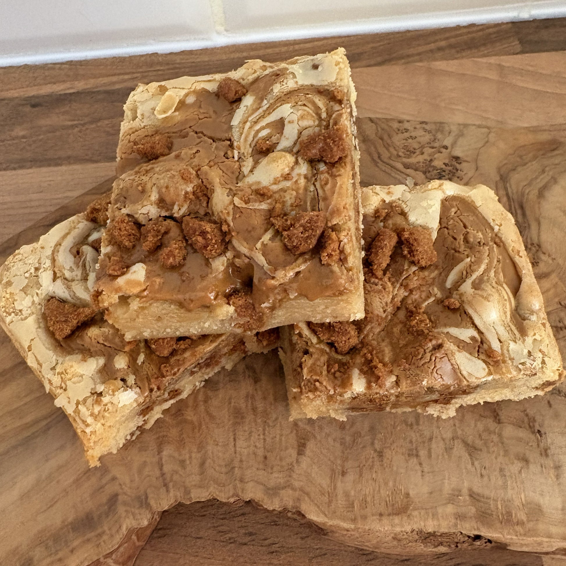 Three square pieces of biscoff blondie  on a wooden surface.