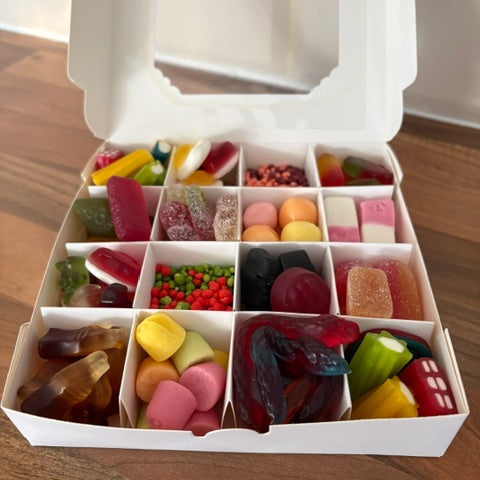 A white cardboard gift box filled with assorted colorful candies and gummy sweets, photographed on a wooden surface.