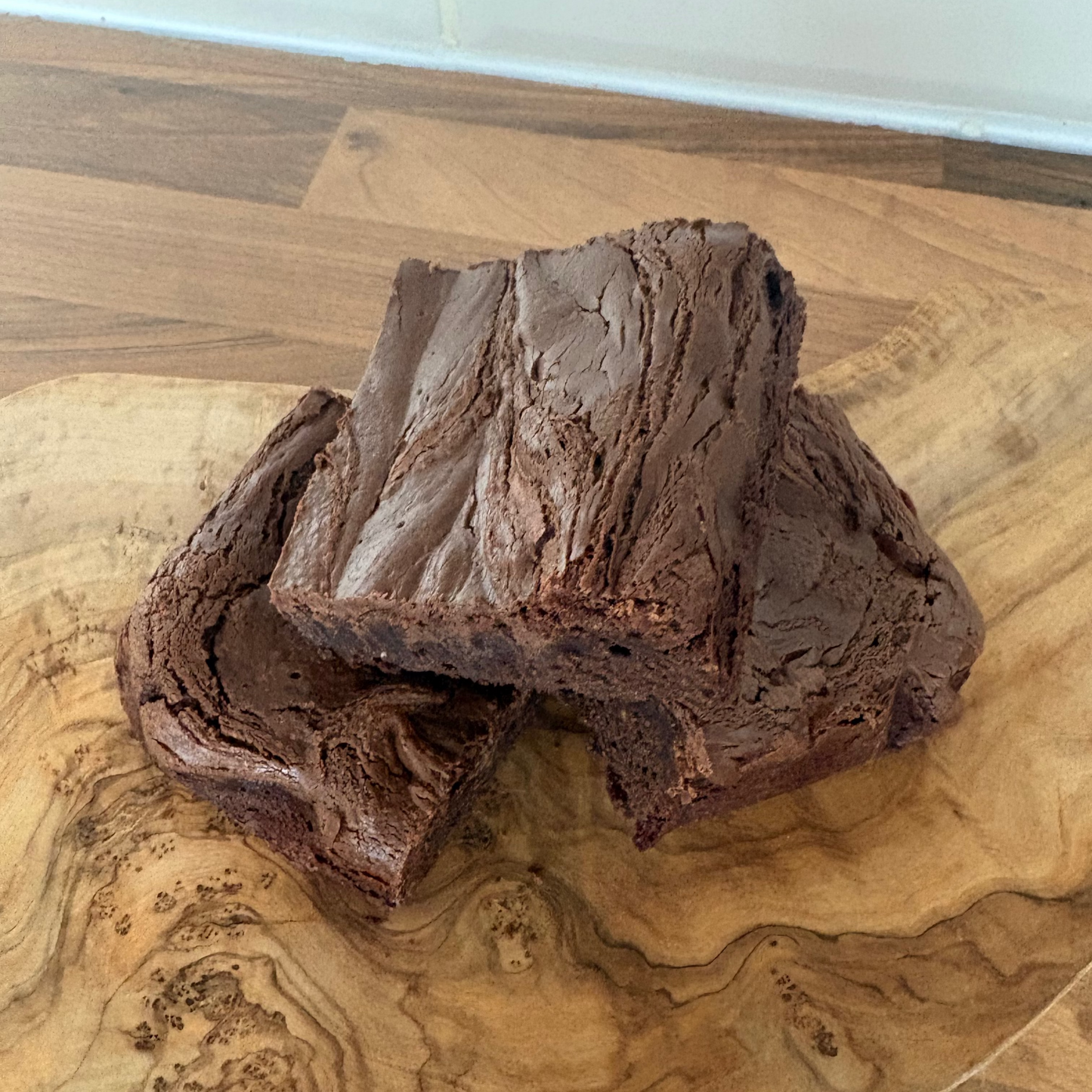 Two chocolate brownies on a wooden cutting board