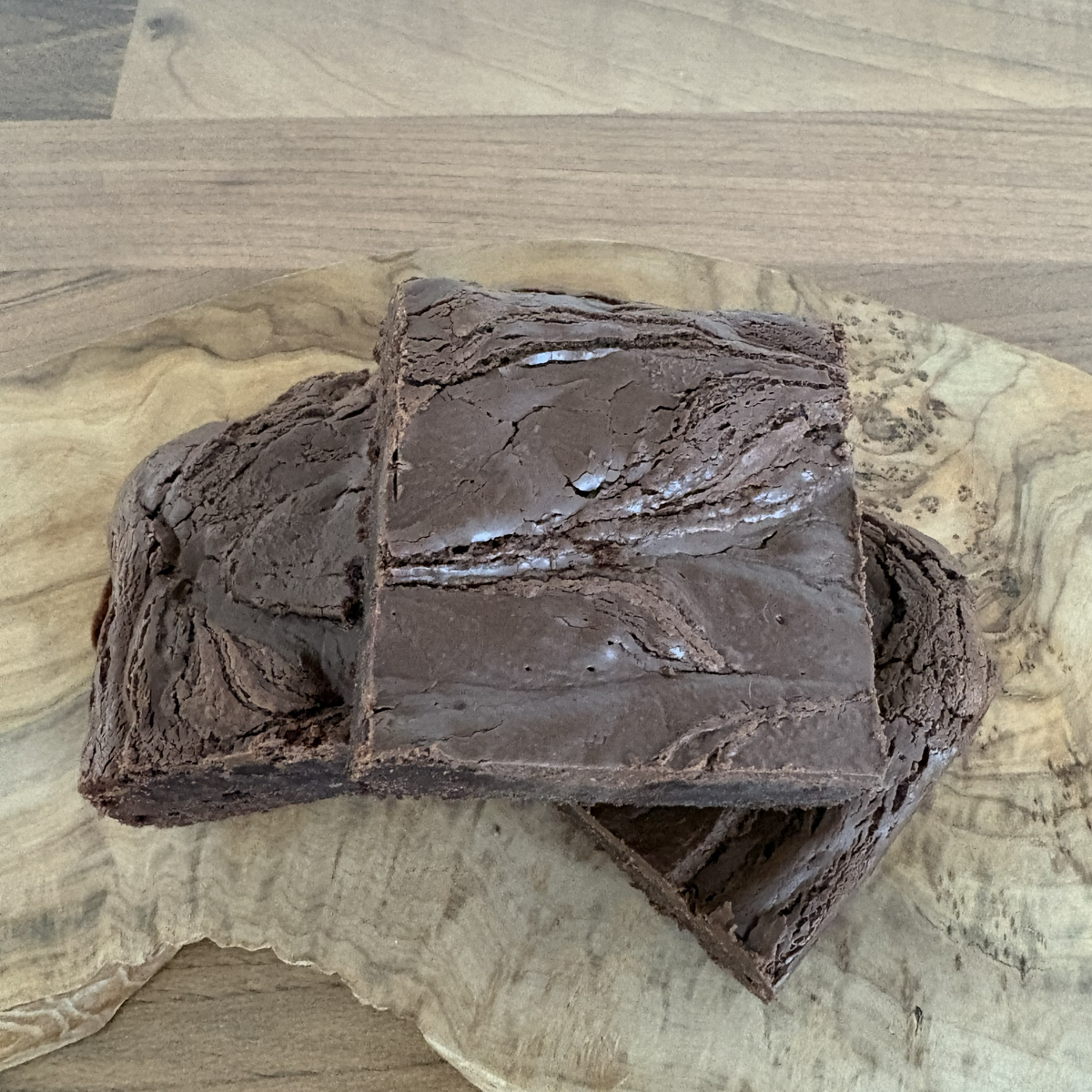 Two chocolate brownies on a wooden cutting board