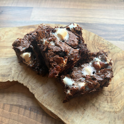 Three pieces of chocolate brownie with marshmallows resting on a rustic wooden cutting board.