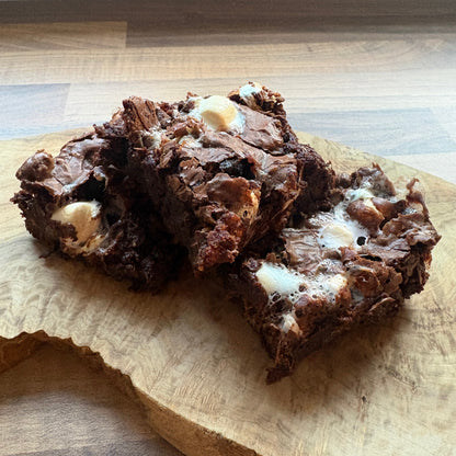 Two rich, dark chocolate rocky road brownies with marshmallow and chocolate digestive chunks, stacked on a rustic wooden cutting board.